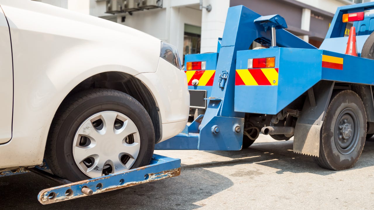 White car being towed away by blue tow truck