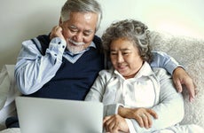 Loving Asian elderly cheerful couple using laptop computer in bed.