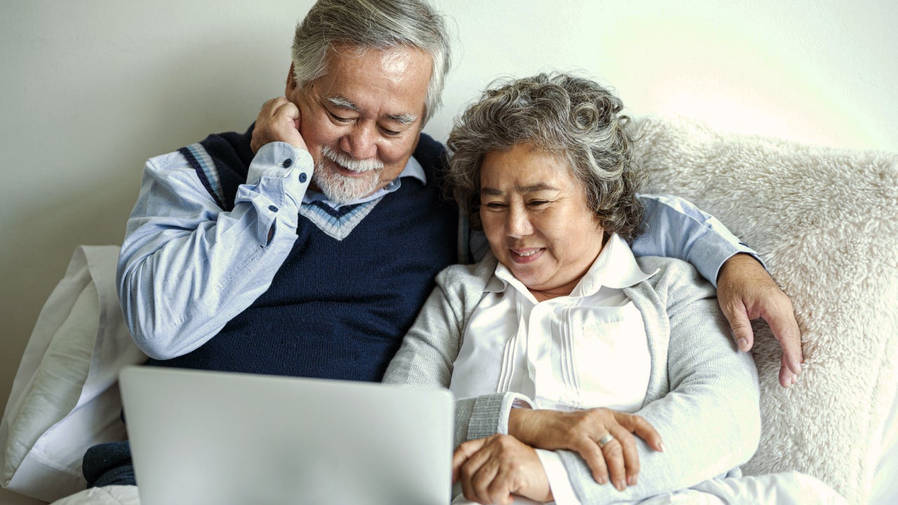 Loving Asian elderly cheerful couple using laptop computer in bed.