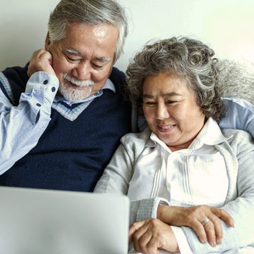 Loving Asian elderly cheerful couple using laptop computer in bed.