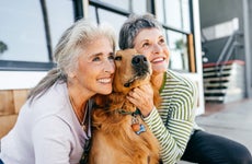 Two older ladies pose for a picture next to their golden retriever.