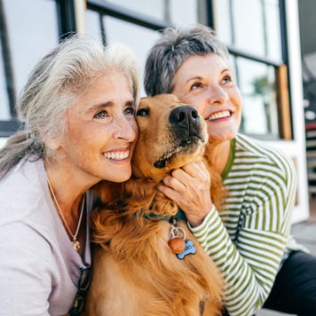 Two older ladies pose for a picture next to their golden retriever.
