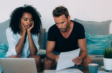 A stressed out woman and man look over bills while sitting on a couch.