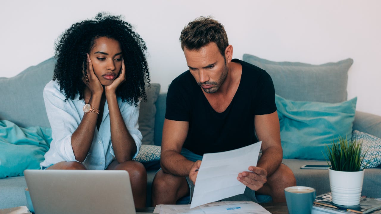 A stressed out woman and man look over bills while sitting on a couch.