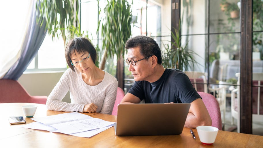 Older Asian couple sits at the kitchen table going over their finances.