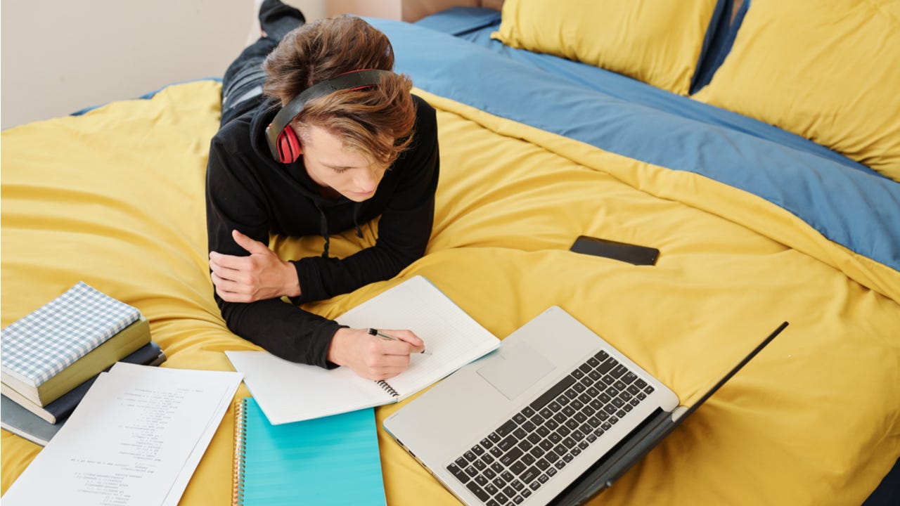 High school student studies on a bed