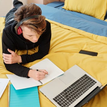 High school student studies on a bed