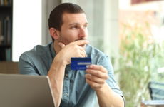 Man looks out window while holding a credit card