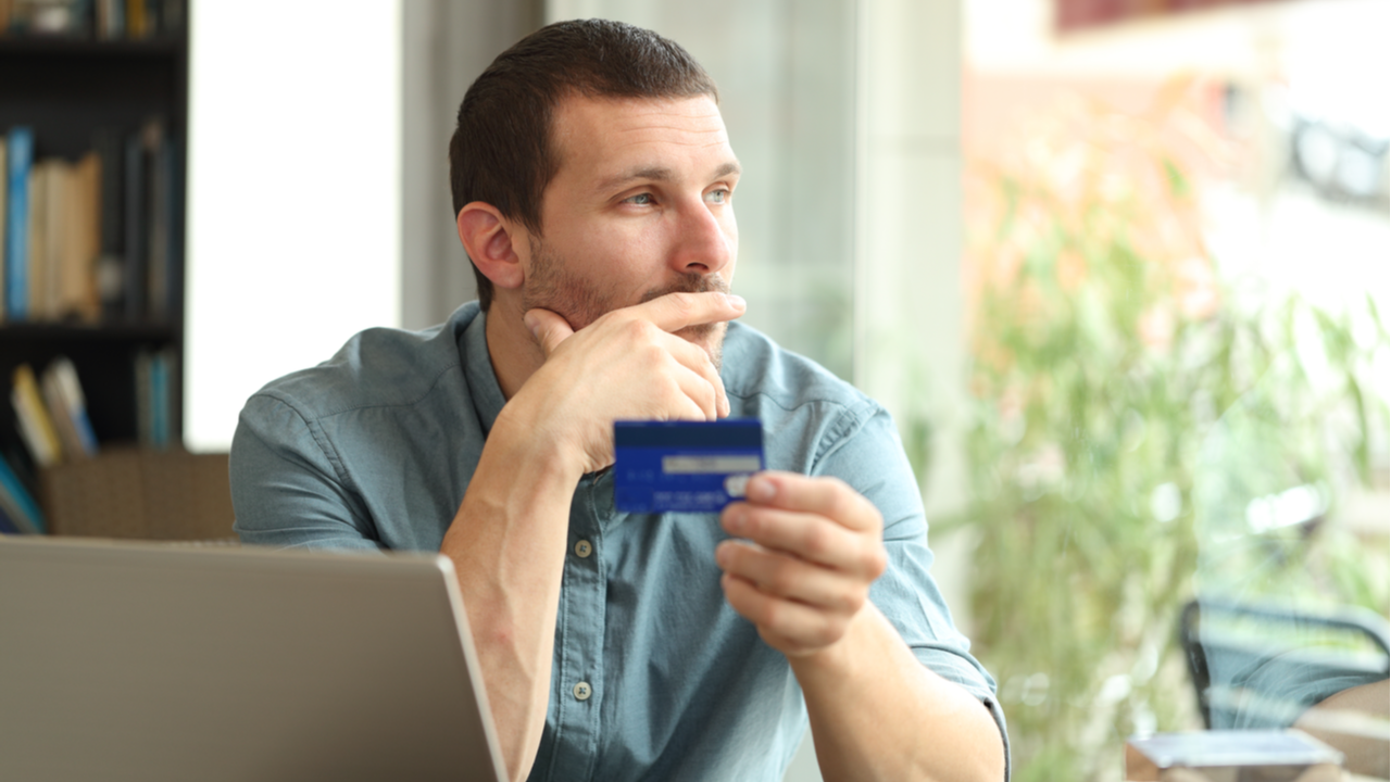 Man looks out window while holding a credit card