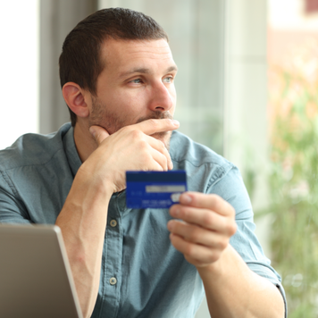 Man looks out window while holding a credit card