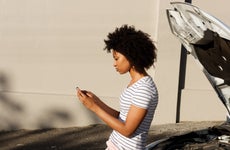 Woman looks at phone during car breakdown.