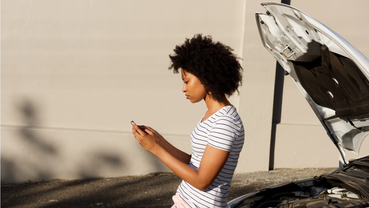 Woman looks at phone during car breakdown.