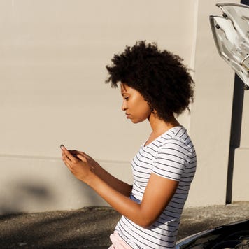 Woman looks at phone during car breakdown.