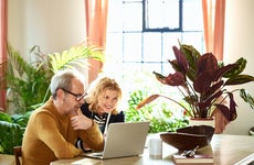 Man and woman looking at laptop sitting on table with vibrant background including several large house plants