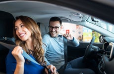 Couple sitting in car putting on seatbelts, smiling towards the back seat