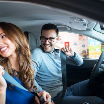 Couple sitting in car putting on seatbelts, smiling towards the back seat