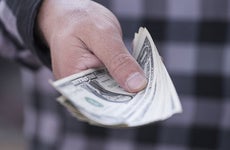 Man in plaid shirt extending hand with dollar bills © Erik Kalibayev/Shutterstock.com