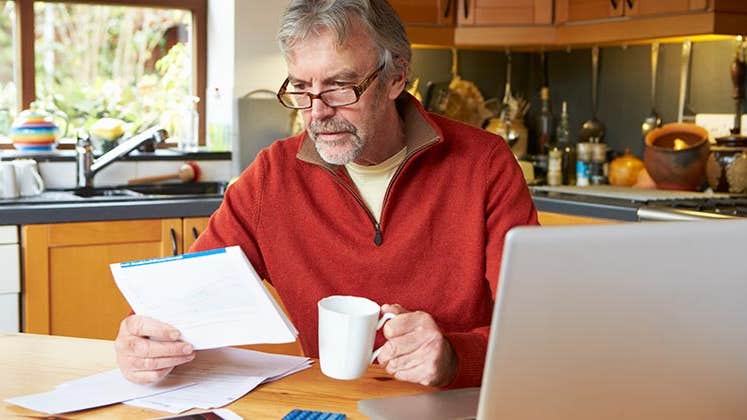 Mature man in red fleece pullover going over finances in kitchen | iStock.com/omgimages
