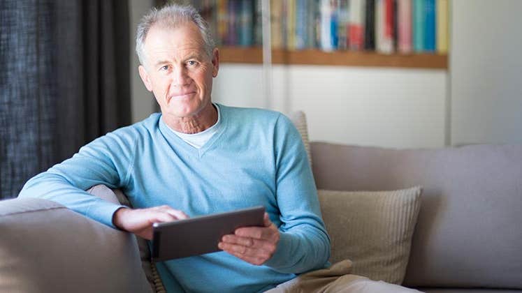 Senior male in light blue sweater browsing tablet | Alistair Berg/DigitalVision/Getty Images