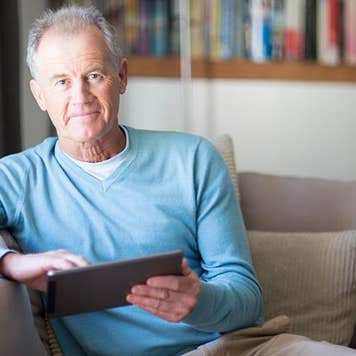 Senior male in light blue sweater browsing tablet | Alistair Berg/DigitalVision/Getty Images