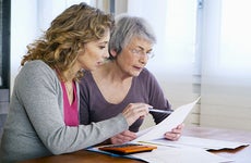 Senior woman sitting at table with younger woman looking at paperwork © Image Point Fr/Shutterstock.com