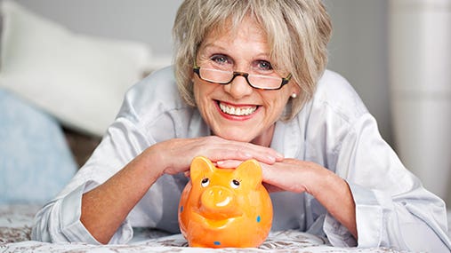 Happy senior woman posing with orange piggy bank © racorn/Shutterstock.com