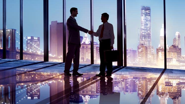 Businessmen shaking hands in front of cityscape © Rawpixel/Shutterstock.com