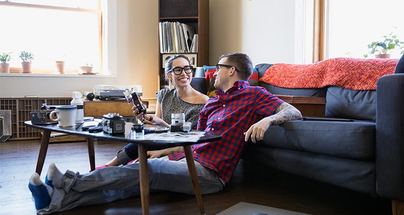 Smiling millennial couple sitting on living room floor | Hero Images/Getty Images