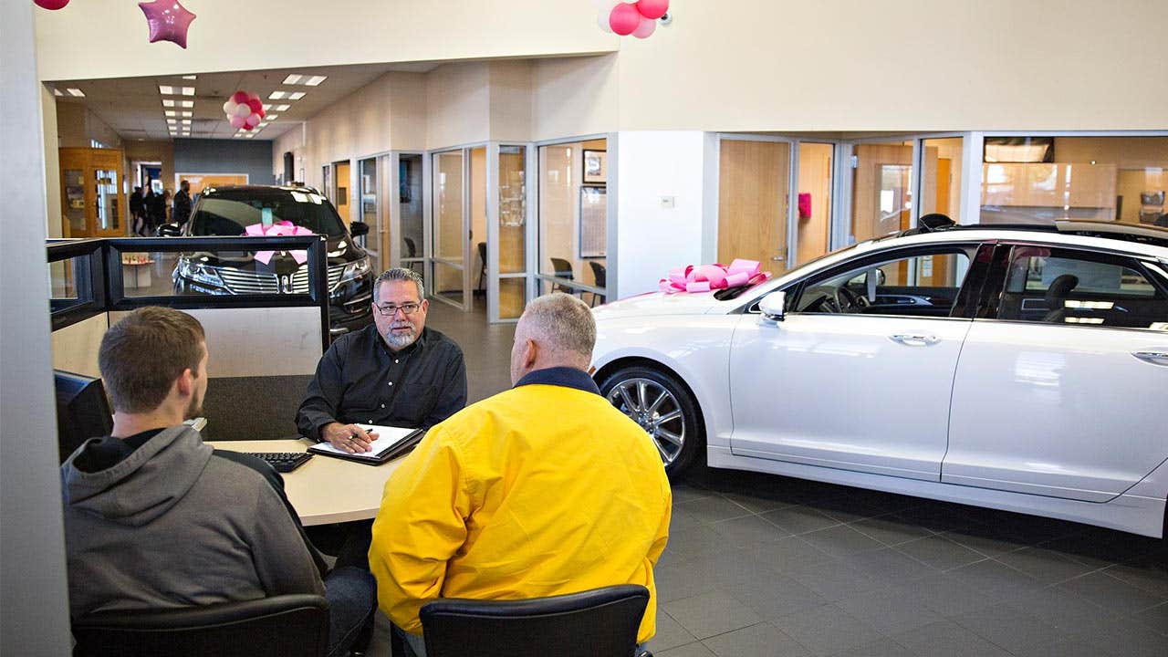 Two men sitting with car dealer, negotiating price