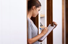 Woman leaning against doorframe with clipboard, writing © iStock