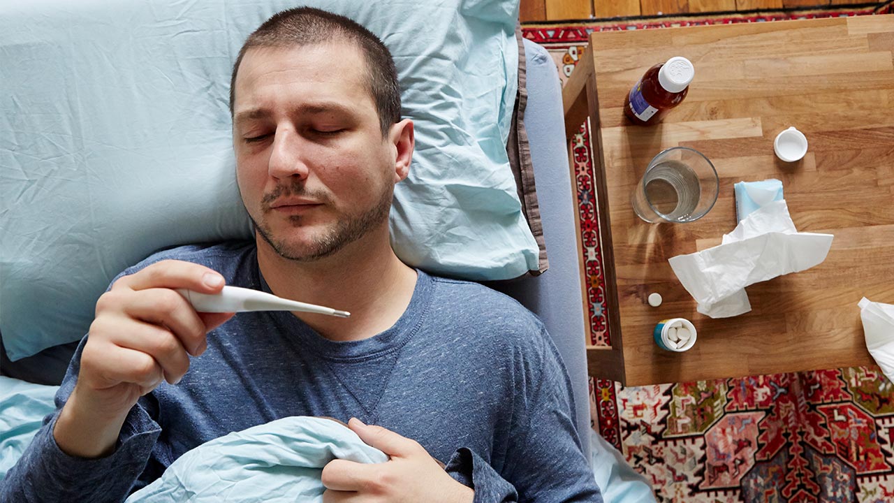 Man feeling sick in bed, checking thermometer