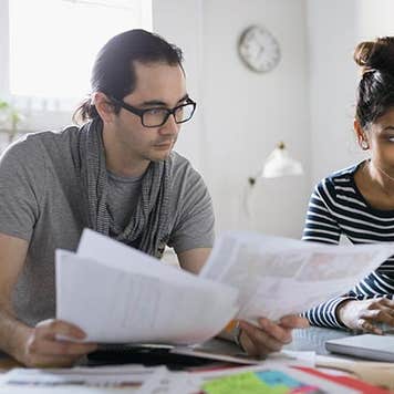 Man and woman reading documents and browsing on laptop | Hero Images/Getty Images
