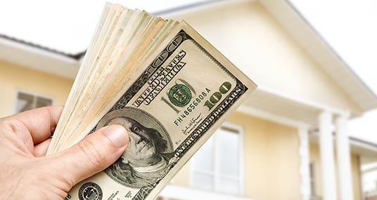 Close up of a hand holding cash in front of a house © Kuzma/Shutterstock.com