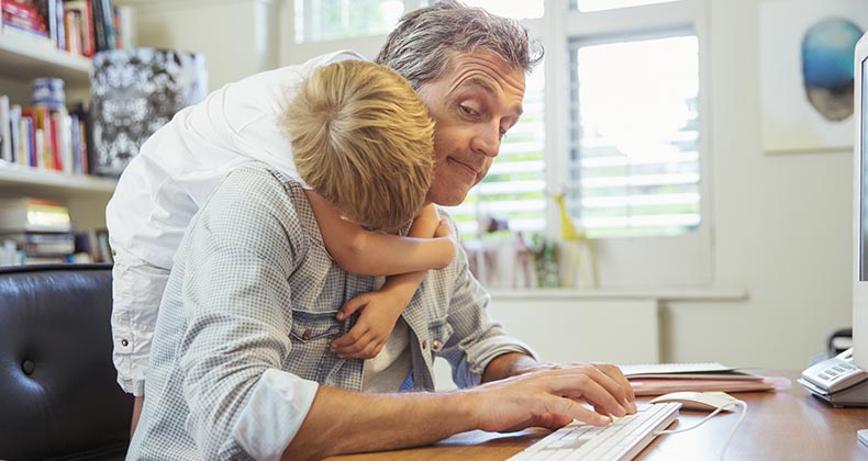 Young son hugging dad working from home office | Paul Bradbury/Getty Images