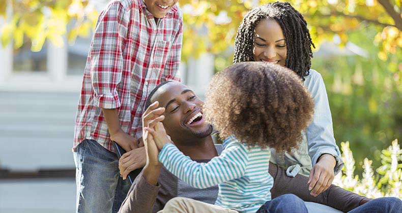 Young family laughing and hugging outdoors | Paul Bradbury/Getty Images