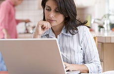 Woman in the kitchen using a laptop with man in the background © Monkey Business - Fotolia.com