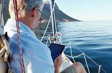 Older man sitting on boat with tablet © Warren Goldswain/Shutterstock.com