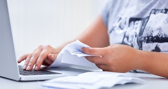 Woman doing paperwork on laptop © Singkham/Shutterstock.com