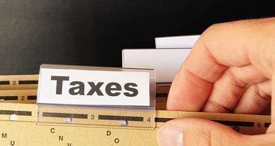 Male hand holding folder with tab labeled "Taxes" © gunnar3000 - Fotolia.com