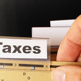 Male hand holding folder with tab labeled "Taxes" © gunnar3000 - Fotolia.com
