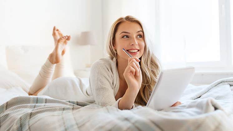 Woman writing notes on bed | Syda Productions/Shutterstock.com