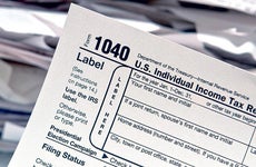 1040 tax forms with stacks of papers on background © Olivier Le Queinec/Shutterstock.com