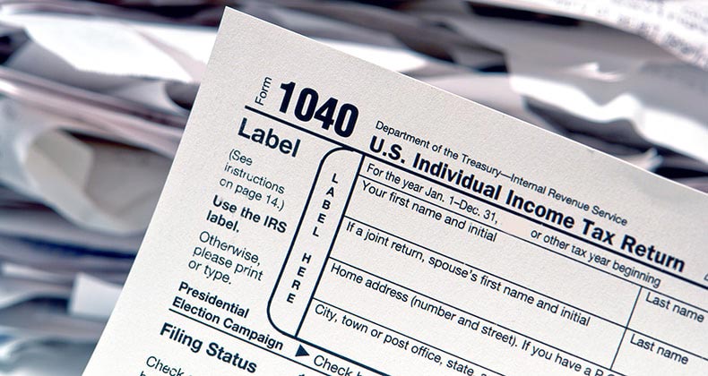 1040 tax forms with stacks of papers on background © Olivier Le Queinec/Shutterstock.com