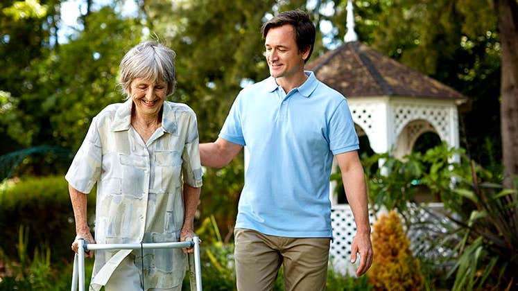 Adult son walking with senior parent in a walker | Morsa Images/Getty Images