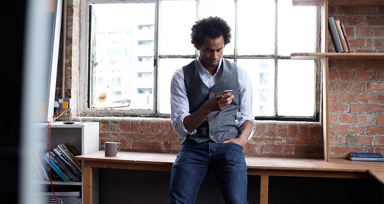 Man leaning against desk, looking at phone | Lilly Roadstones/Getty Images