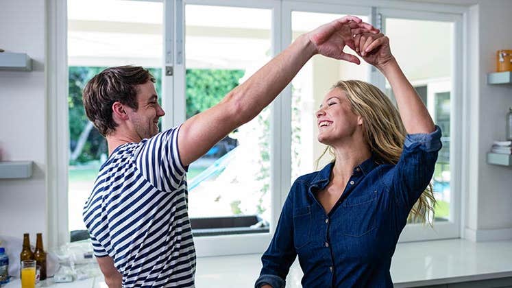 Young couple laughing and dancing together in kitchen | wavebreakmedia/Shutterstock.com
