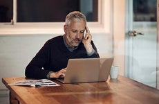 Mature man in dining room reading laptop | iStock.com/PeopleImages