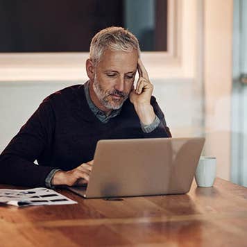 Mature man in dining room reading laptop | iStock.com/PeopleImages