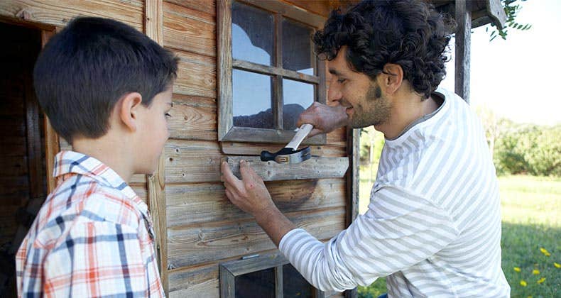 Father hammering wood onto cabin with son | Maria Teijeiro/Getty Images