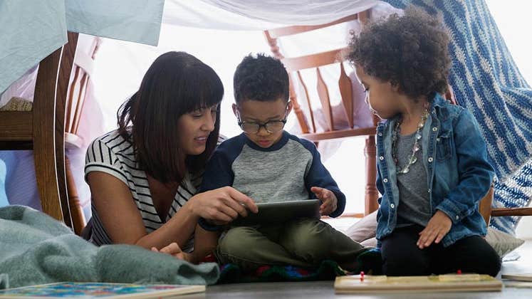 Mother reading to her sons, under a blanket fort | Hero Images/Getty Images